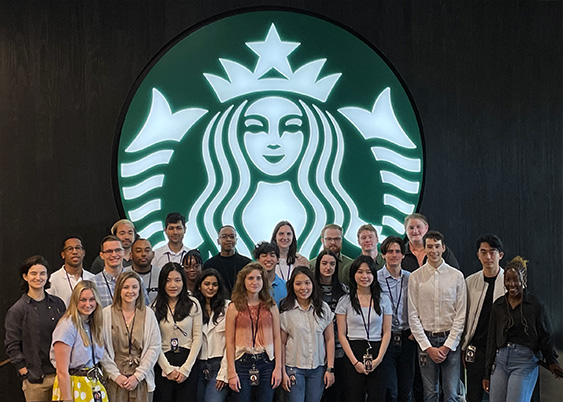 Starbucks interns stand in front of the Starbucks Siren logo at the Seattle headquarters. 