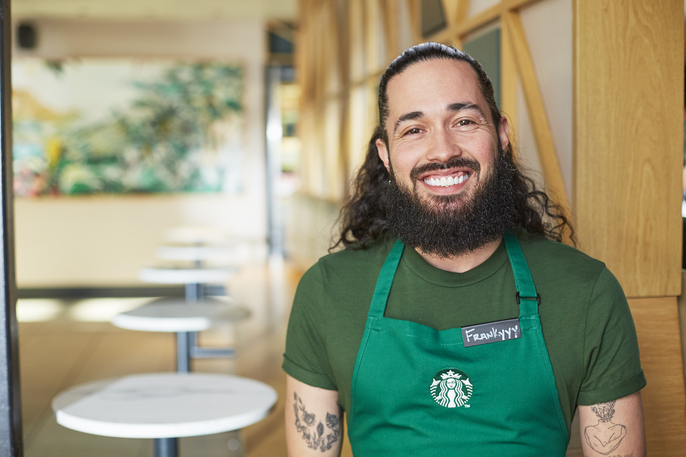 A person wearing a Starbucks green apron smiles directly into the camera.