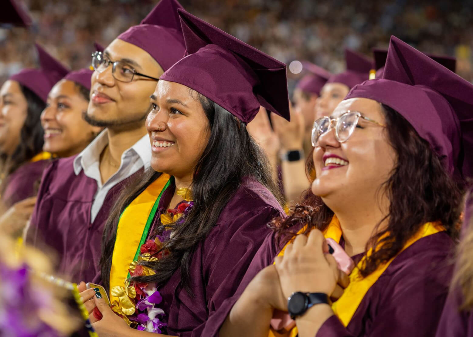 A group of people sit at a commencement ceremony, smiling and wearing maroon ASU cap and gowns.