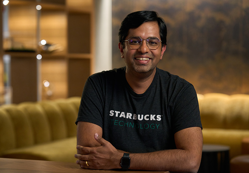 A person wearing a black shirt with "Starbucks" written on it, smiles at the camera.