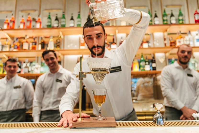 A person stands at a Milan Roastery bar, using a siphon to create a handcrafted mixologist beverage.
