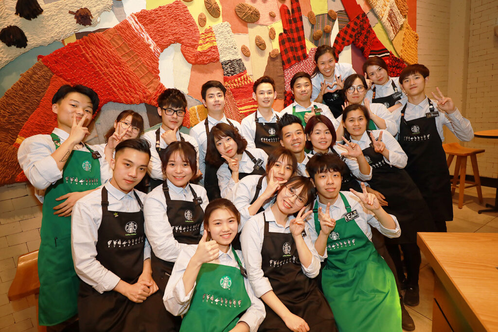 A group of individuals stand together, posing while wearing Starbucks green aprons at the Starbucks Signing store in China