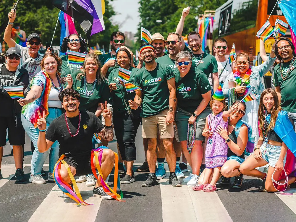 A group of people at an outdoor city parade, walking while holding a Starbucks Pride Network banner.
