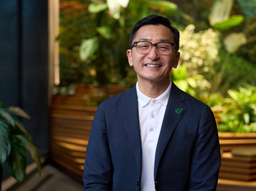 A person smiles in front of a lush green living wall in an office building.