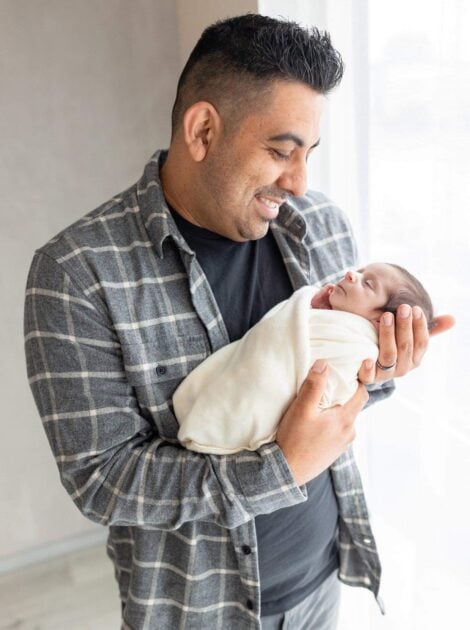 A person holding a newborn baby smiles with adoration at the little one.