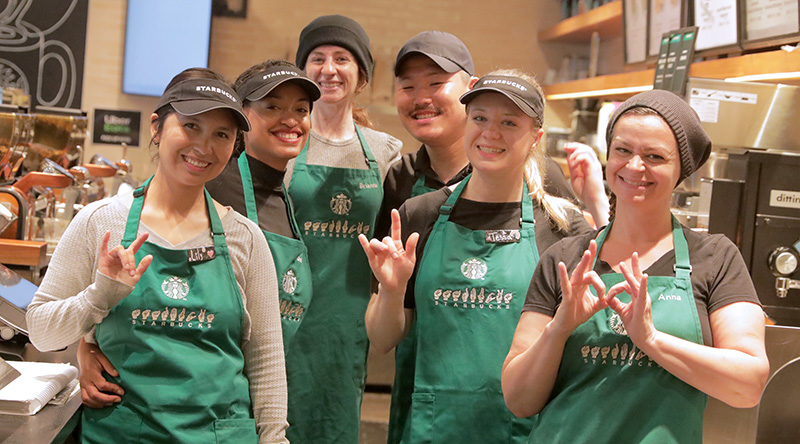 Starbucks partners in an inclusive designed store sign to each other with ASL.