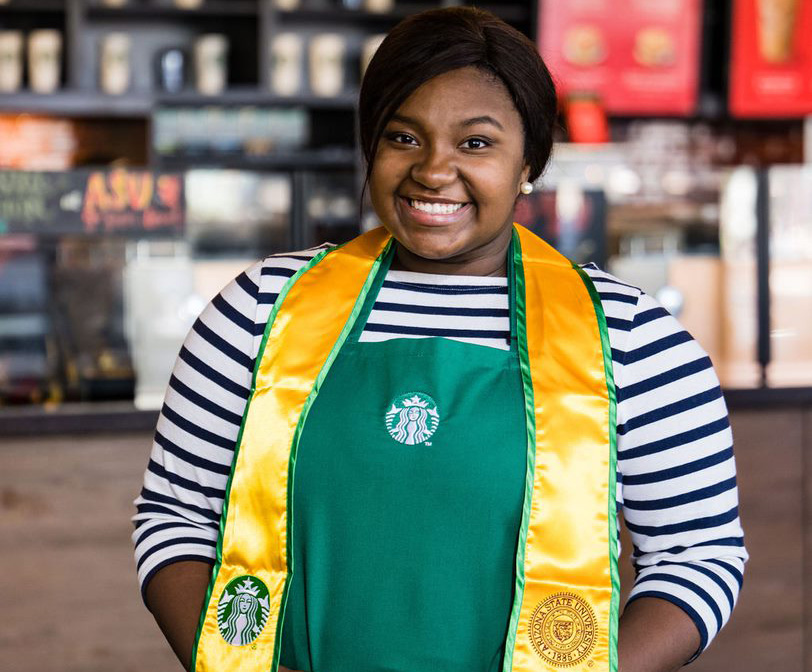 A person wearing an Starbucks Green Apron and ASU Sash smiles into the camera. 