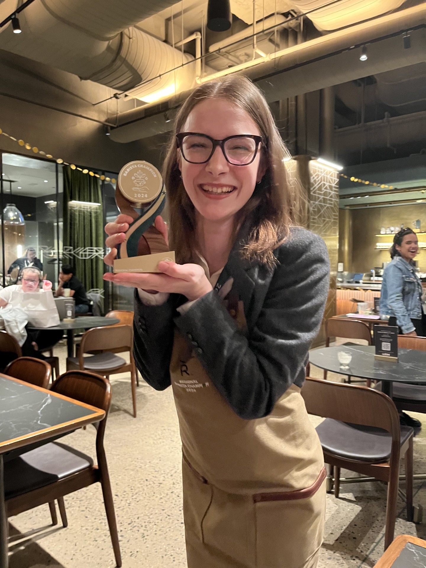 Starbucks partner holds a trophy for regional Starbucks Barista Champion. She smiles at the camera.