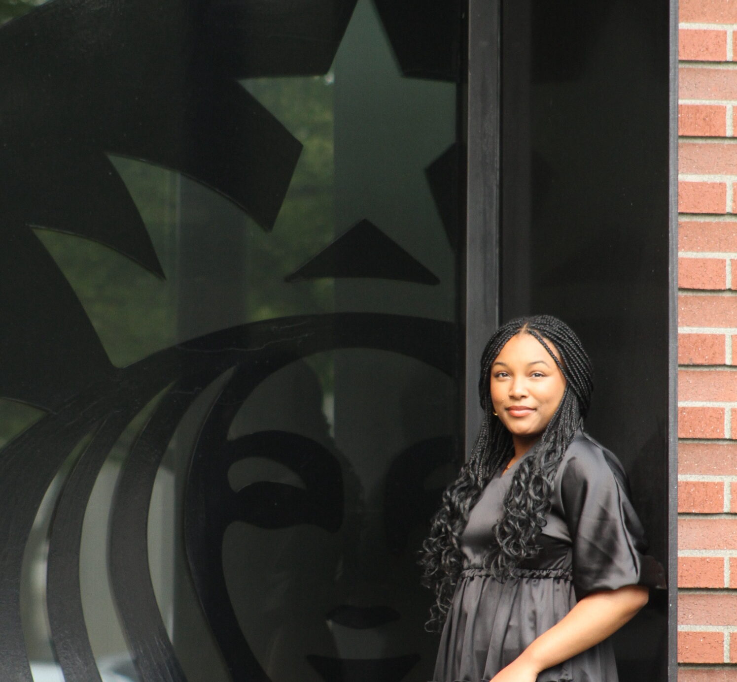 Starbucks intern leans against a brick wall in front of a window with the Starbucks logo.