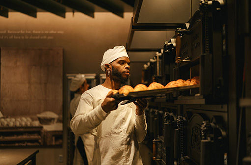 A man wearing white chefs clothing, pulls bread from an industrious oven inside the Starbucks Reserve store.