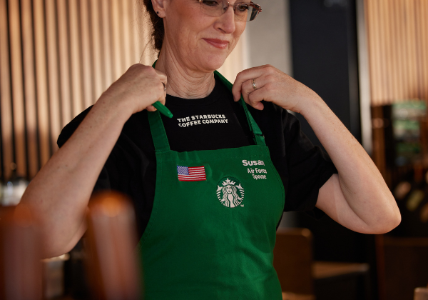 A close up shows a Starbucks barista putting on her green apron. It says her name and has an American flag embroidered onto the apron.