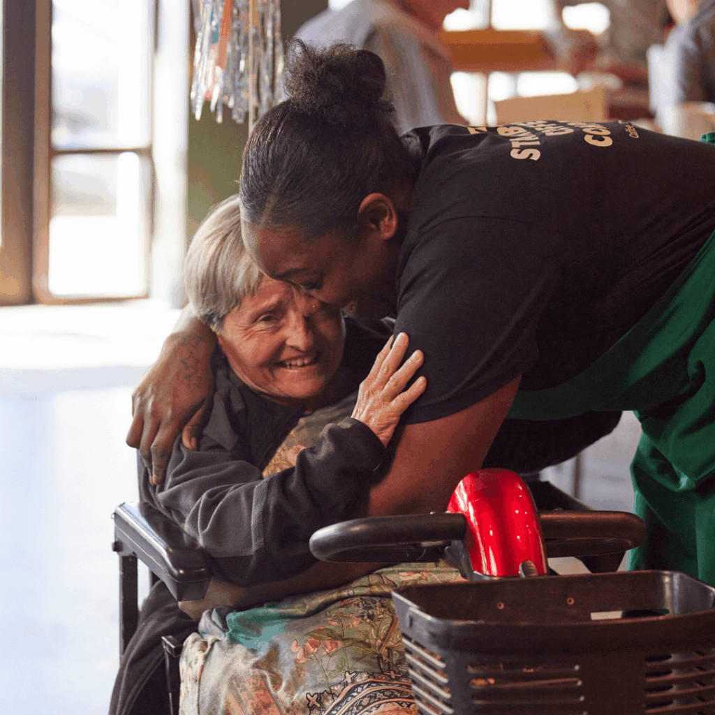 A Starbucks barista leans over and hugs a customer inside a coffeehouse.