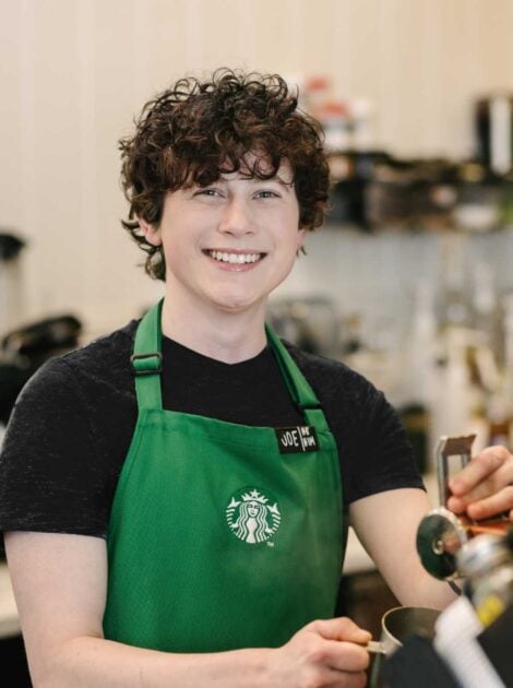 A person wearing a Starbucks green apron smiles directly into the camera.