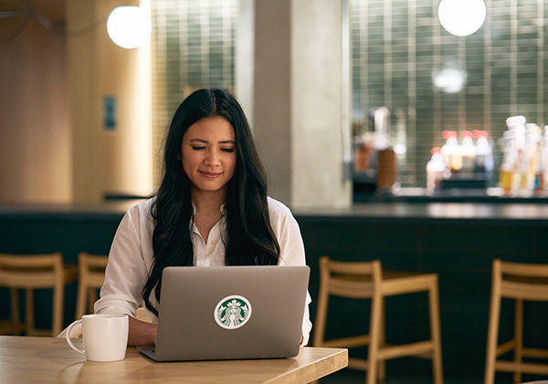 Une personne travaille sur son ordinateur portable, une tasse de café posée à côté d’elle.