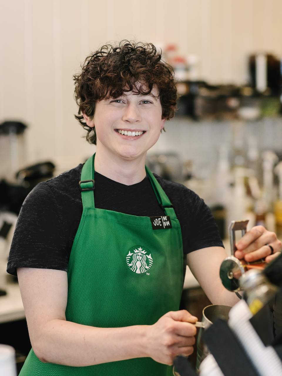 Une personne portant un tablier vert Starbucks se tient derrière le comptoir dans un magasin Starbucks.