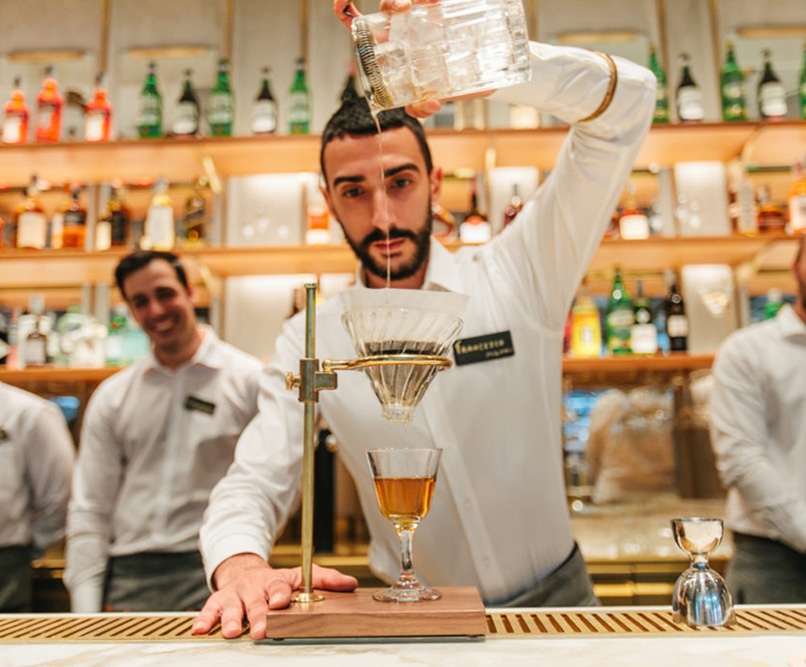 A person stands at a Milan Roastery bar, using a siphon to create a handcrafted mixologist beverage.