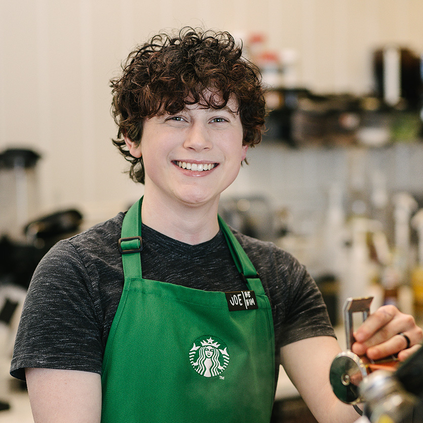 An individual wearing a Starbucks green apron stands behind the counter in a Starbucks store.