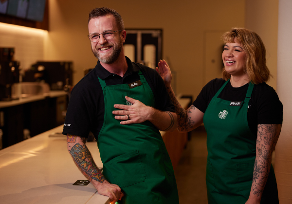 A male and female barista laugh together at a Starbucks coffeehouse.