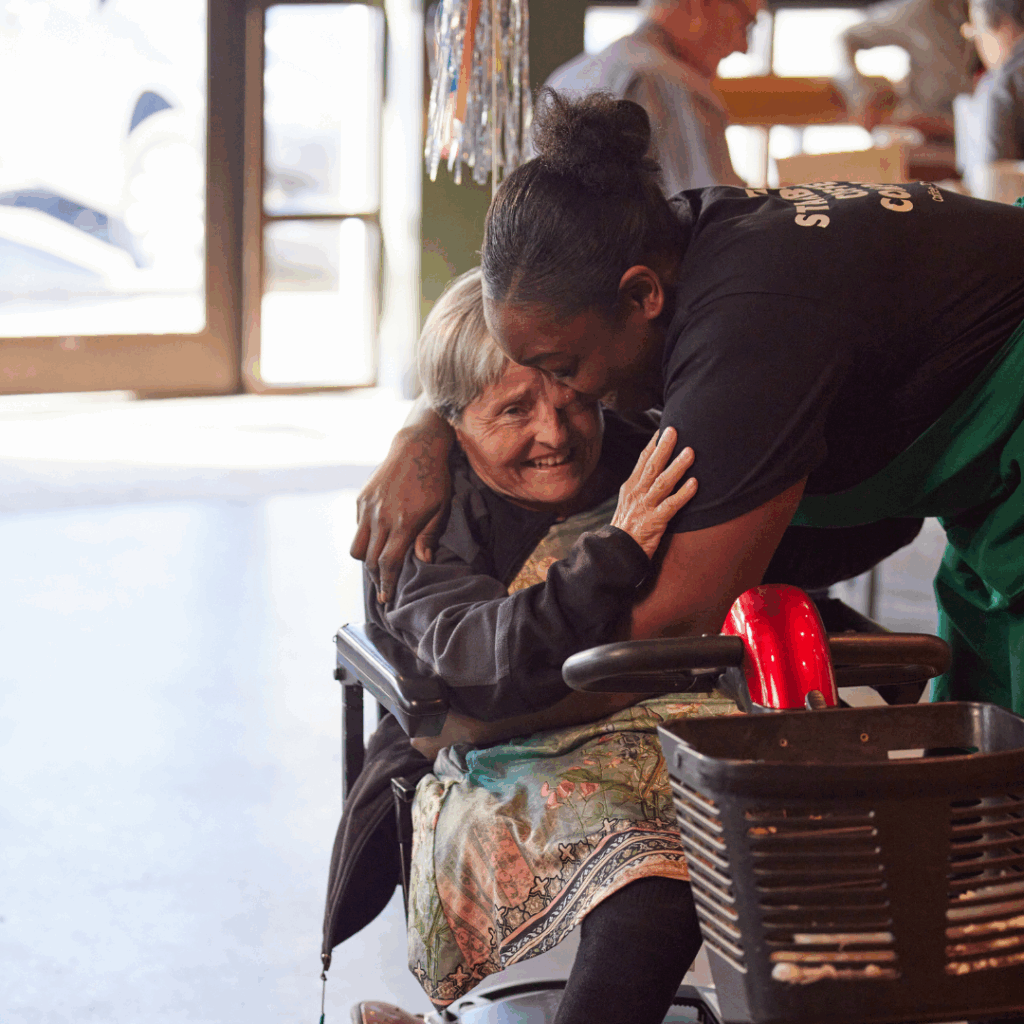 A Starbucks barista leans over and hugs a customer inside a coffeehouse.
