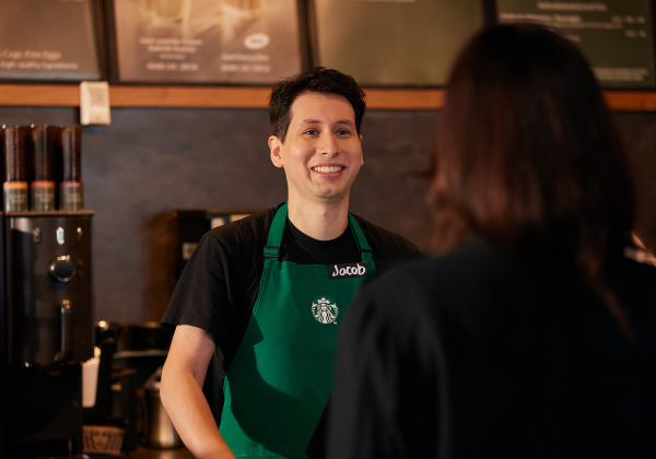 A Starbucks barista smiles at a customer in a coffeehouse.